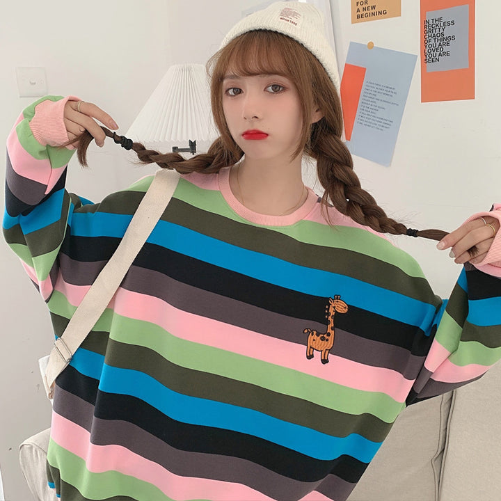A girl wearing a colorful striped sweatshirt with a giraffe design, showcasing a casual fashion style.